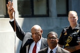 Bill Cosby holds one arm in the air as he leaves court.