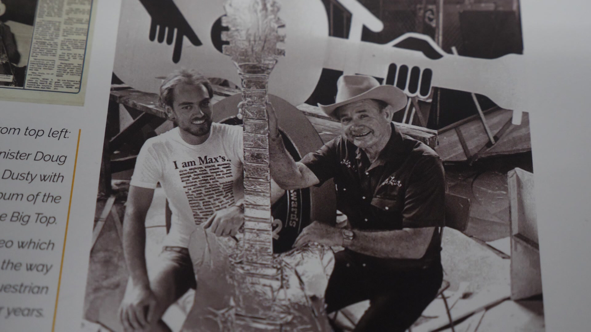 Uma fotografia em preto e branco de dois homens segurando uma guitarra dourada gigante.