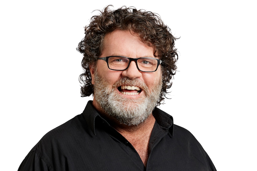 A mid-shot of a smiling Russell Woolf wearing a black collared shirt. 