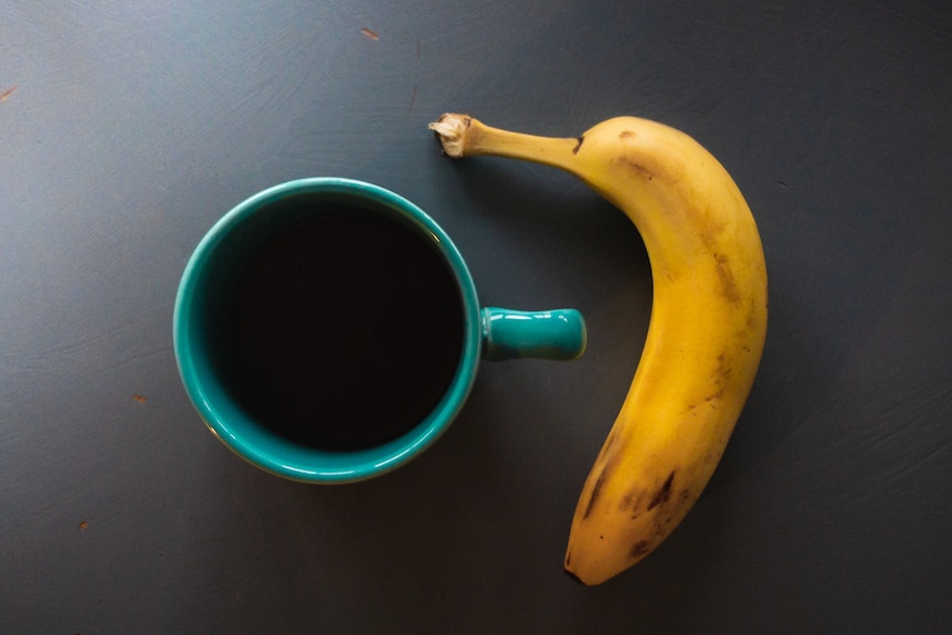 cup of coffee and a banana against a grey background