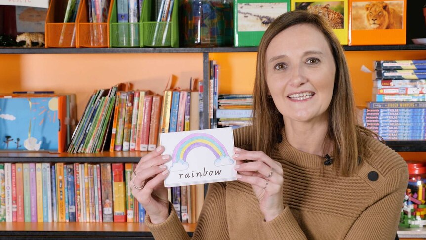 Female teacher holds small card containing rainbow and word "rainbow"