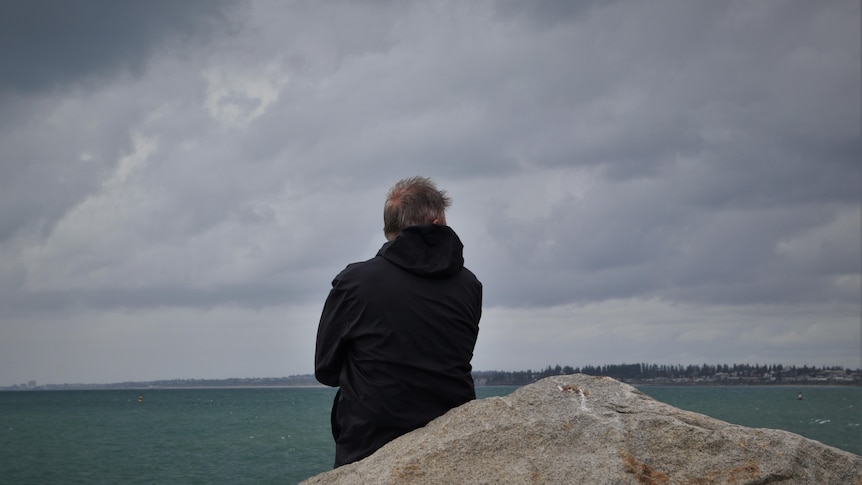 Man sits on dock at fremantle port with stormy sky