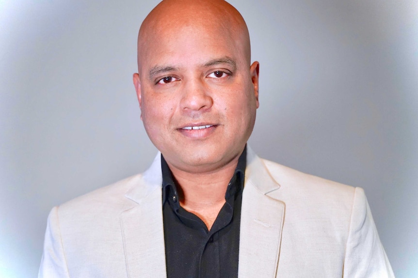 Vikrant Kishore looks into the camera in a close portrait in front of a blank background.