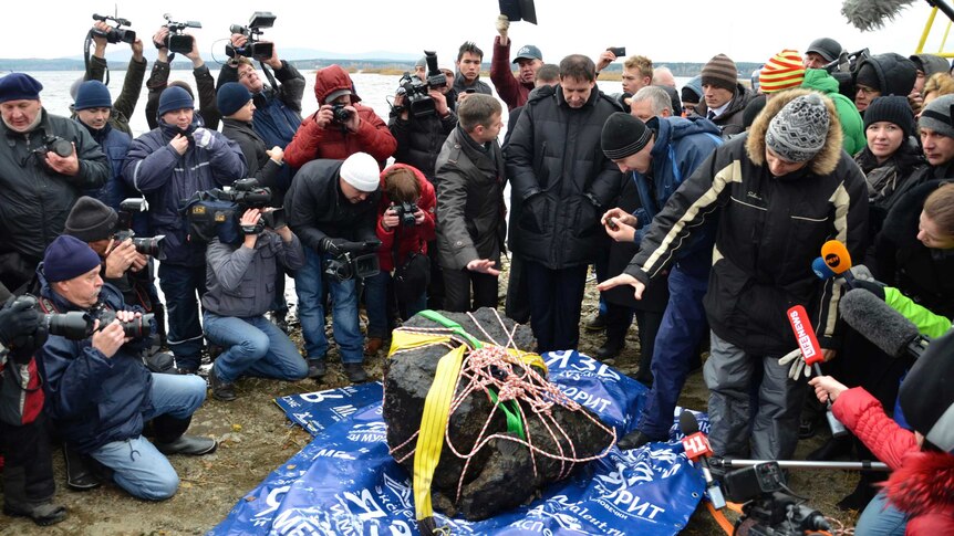 The media gather around a piece of a meteorite on the bank of Lake Chebarkul.