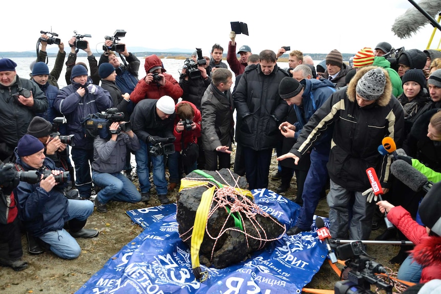 The media gather around a piece of a meteorite on the bank of Lake Chebarkul.