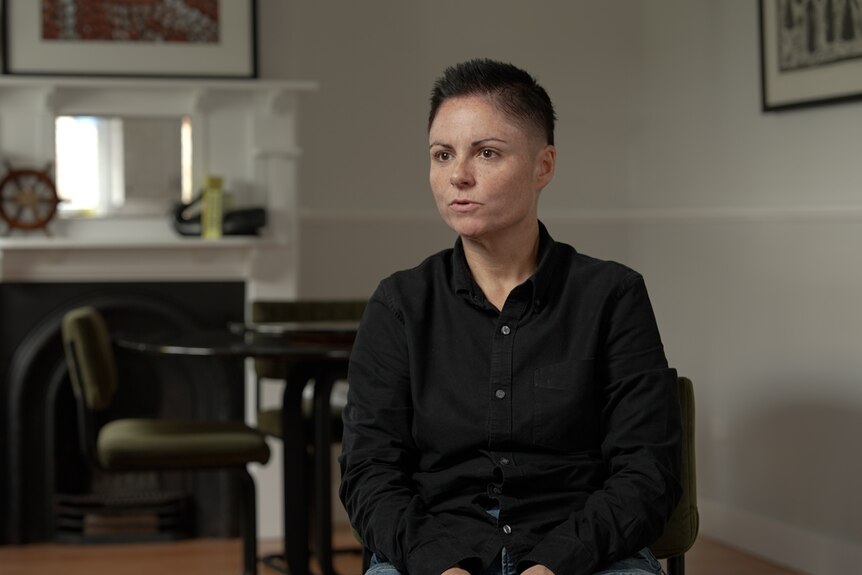a woman with short hair and a black shirt speaking to a camera out of frame
