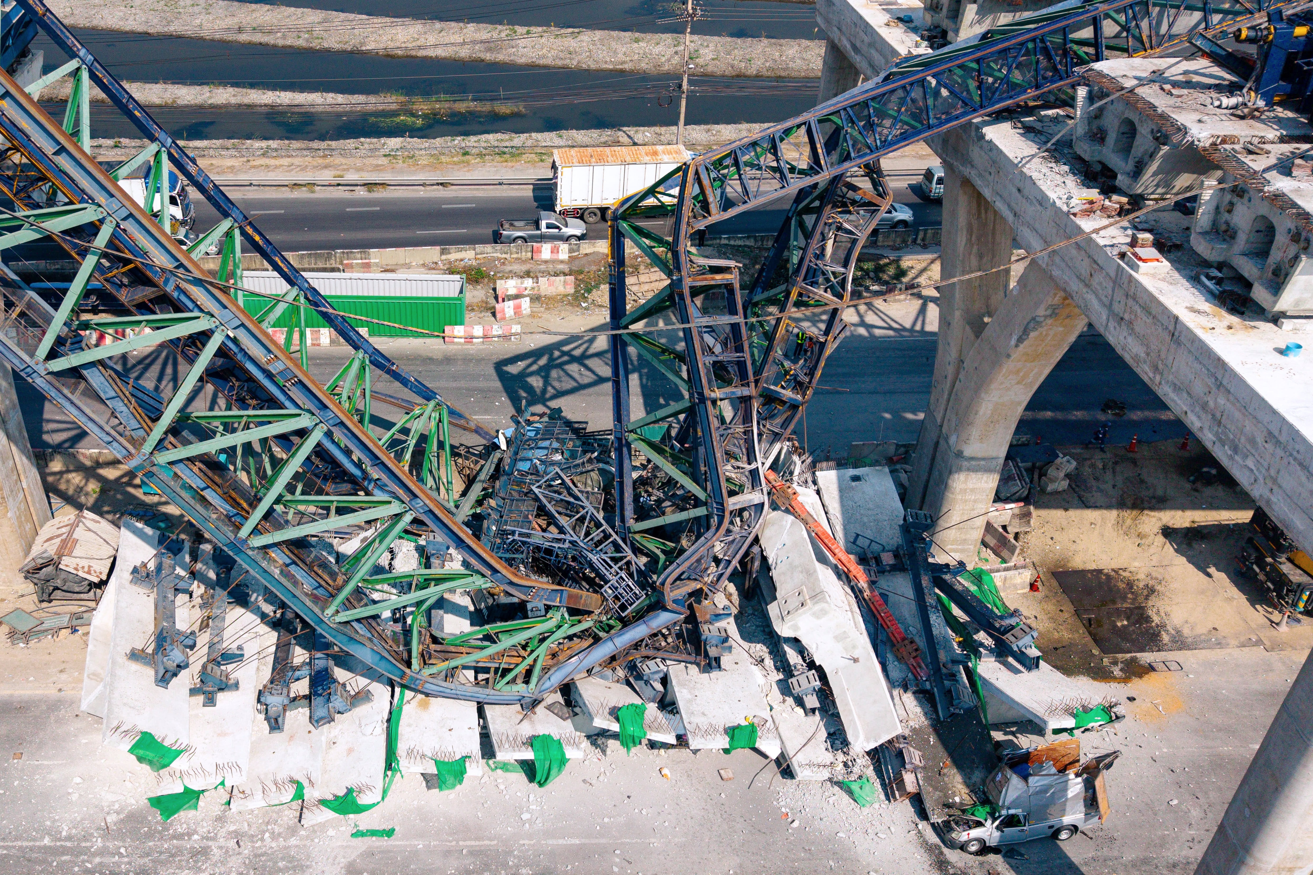 Foto aérea de aço retorcido verde, azul e laranja que caiu em uma estrada entre postes de concreto.