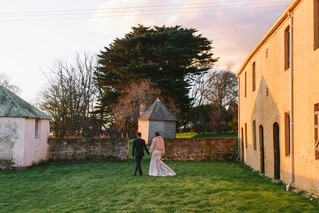 A bride and groom walk among some historic buildings.