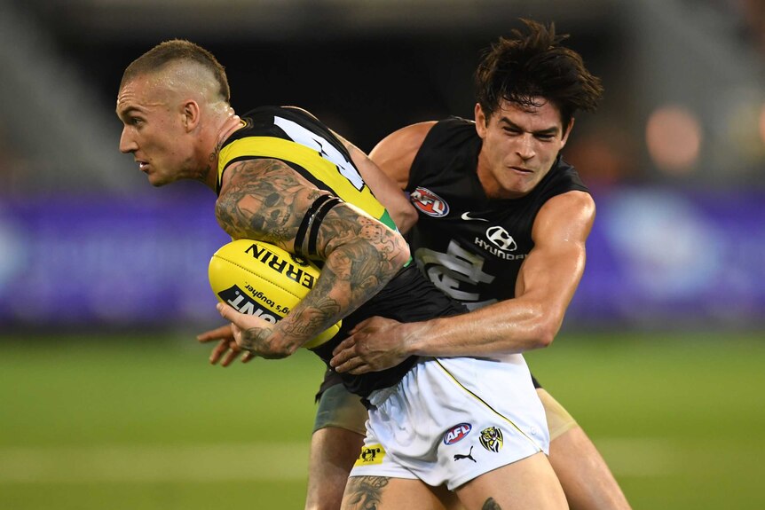 A male Richmond AFL player holds the ball as he is tackled by a Carlton opponent at the MCG.