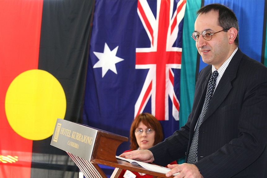 Mike Pezzullo, then acting Defence secretary, stands at a lecturn with flags behind him
