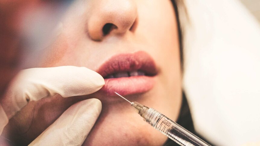 A surgeon injects filler into a young woman's lips