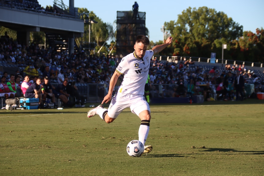 A Macarthur FC player kicks a ball during a match at a stadium .