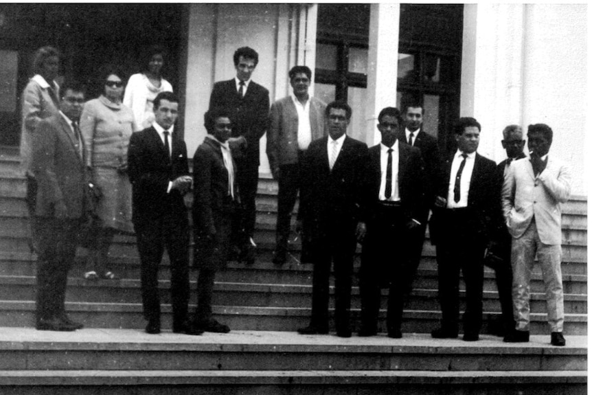 Indigenous men and women stand on the steps of Parliament House in Canberra in an old black and white photo.