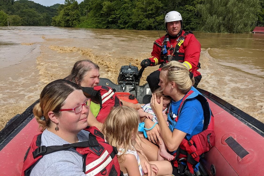 Rescue worker guides small raft with evacuees through flood water.