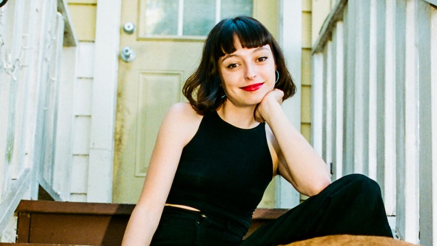A 2019 press shot of Stella Donnelly sitting on doorstep to old house