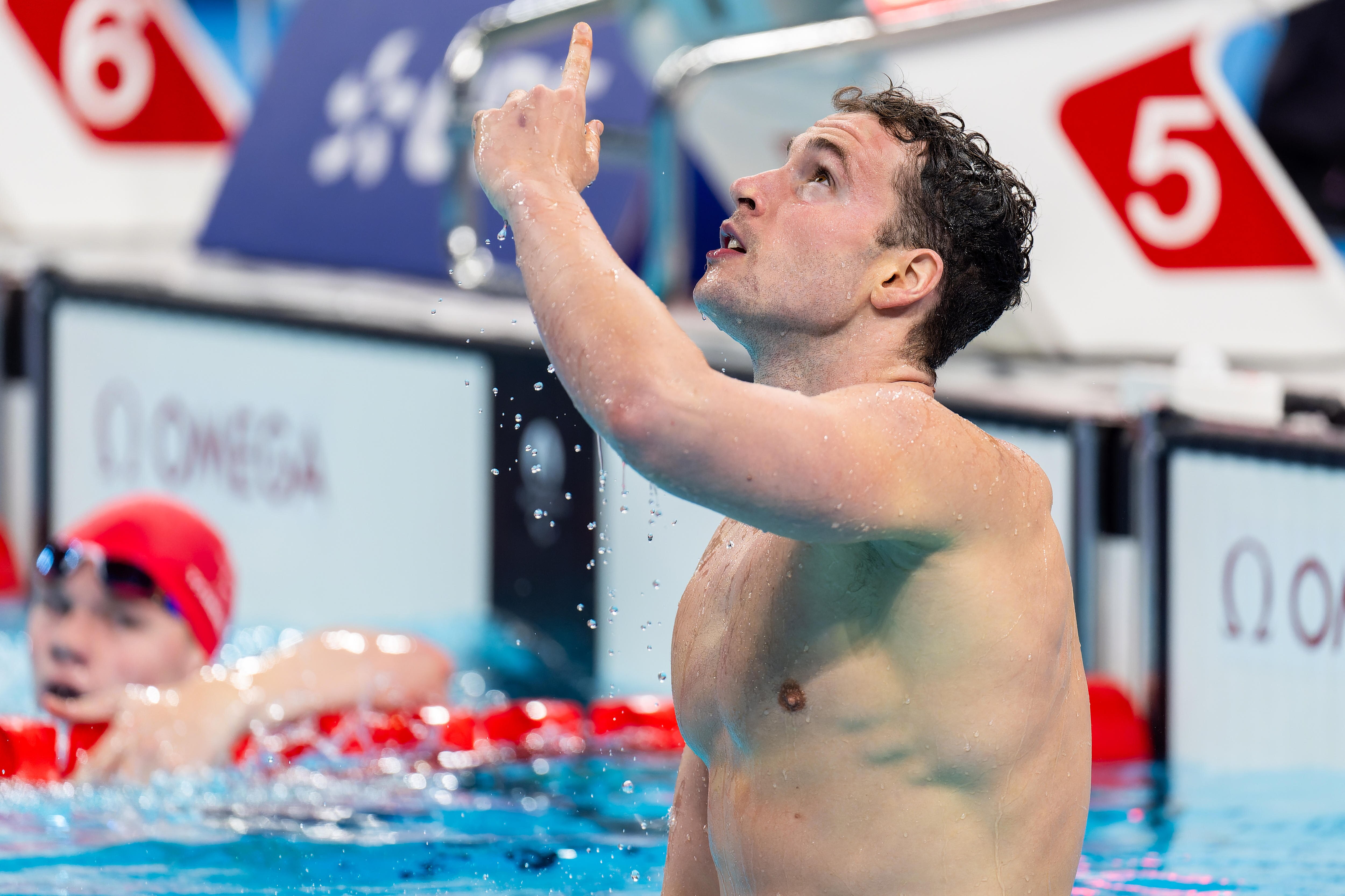 Ben Hance straddles a lane rope and points to the sky after winning a gold medal in the pool