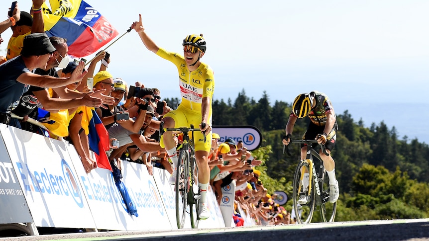 A male cyclist wearing yellow puts his hand in the air