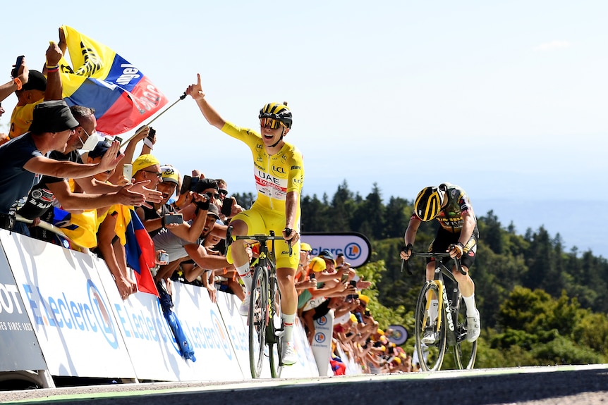 A male cyclist wearing yellow puts his hand in the air
