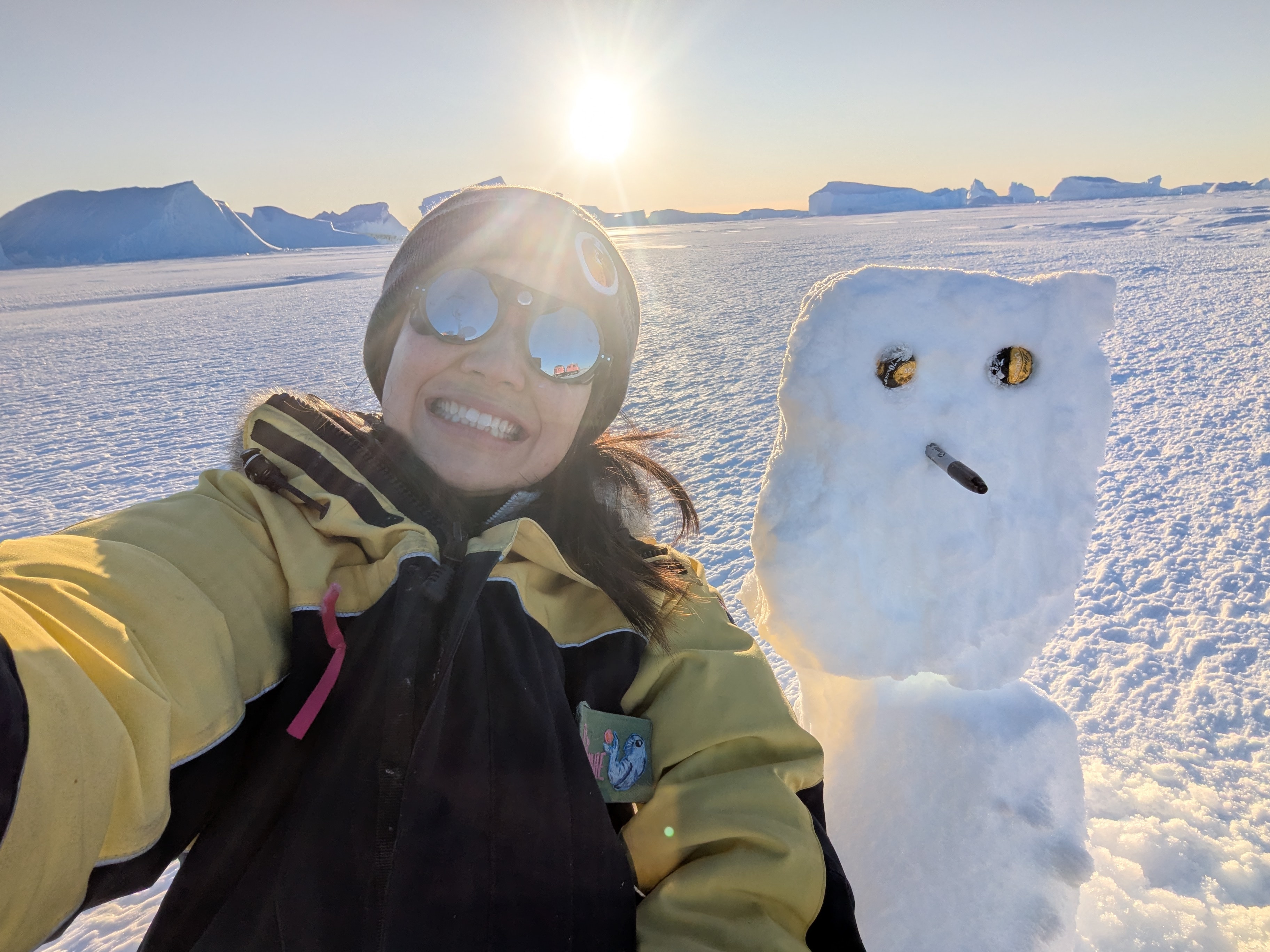Winnie Yum poses for a selfie in the snow, next to a snowman and with the sun setting behind her.
