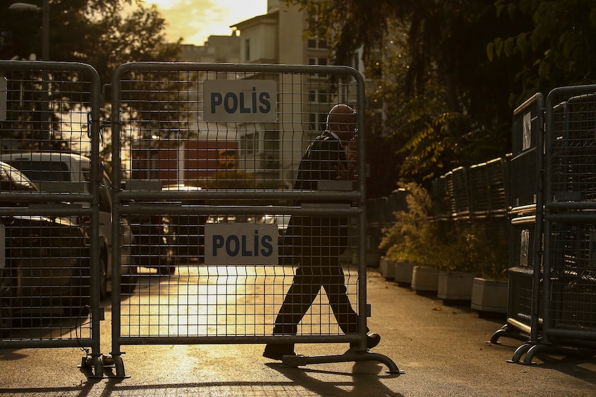 Photograph taken at twilight, as a man in a suit pulls a large metal barrier marked "Polis" closed.