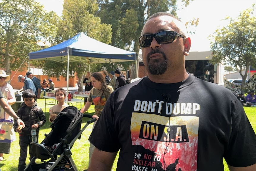 An Indigenous man with a neat beard stands outdoors, looking solemn.