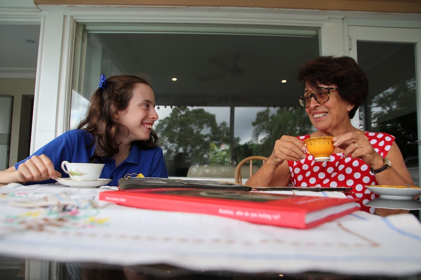 A nonna and a grandaughter laughing as they drink tea