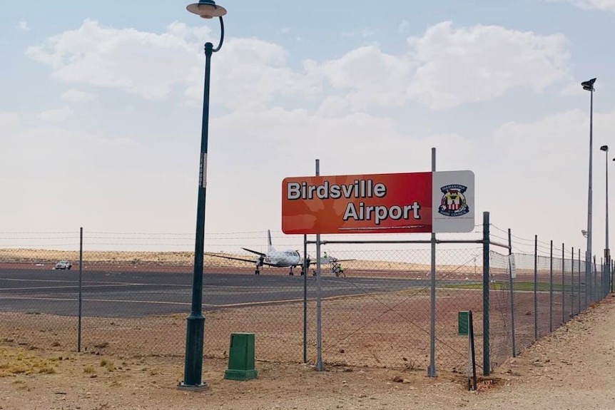 A sign reading 'Birdsville Airport' in front of a landing strip with a small plane on it. 