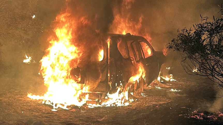 A car is engulfed in flames in the bush.
