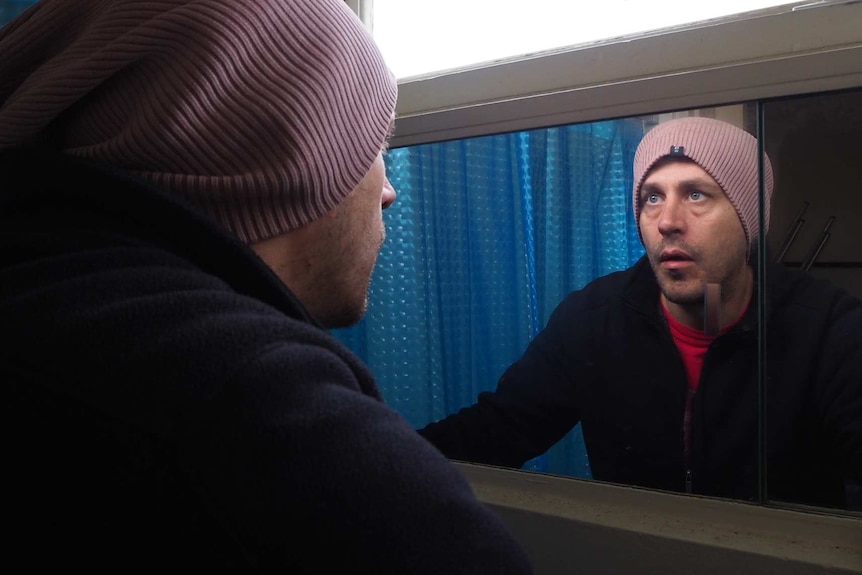 Joel Sinclair looks at his reflection in a mirror.
