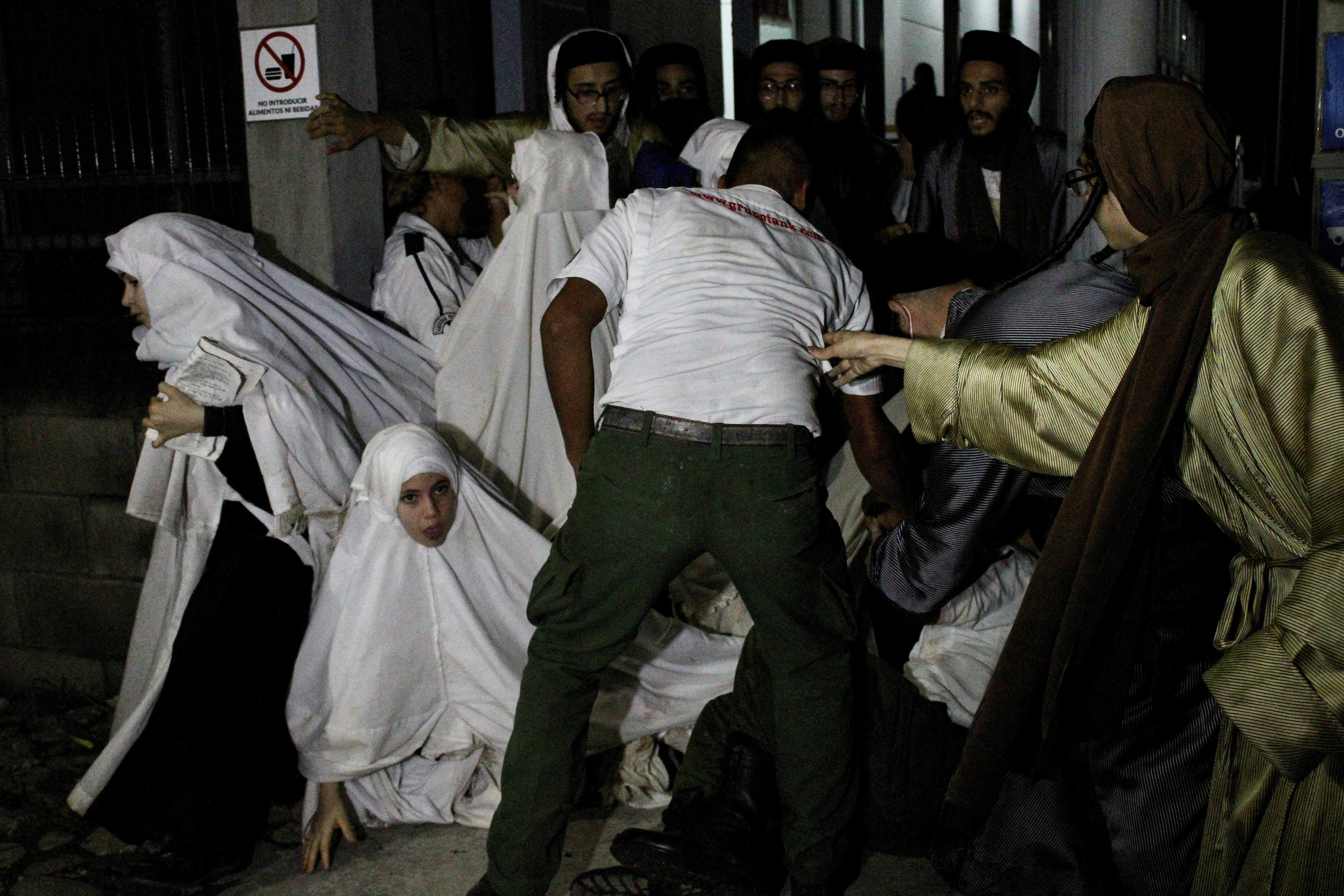 women and girls in white long headcovers and men in robes pull at one another to flee