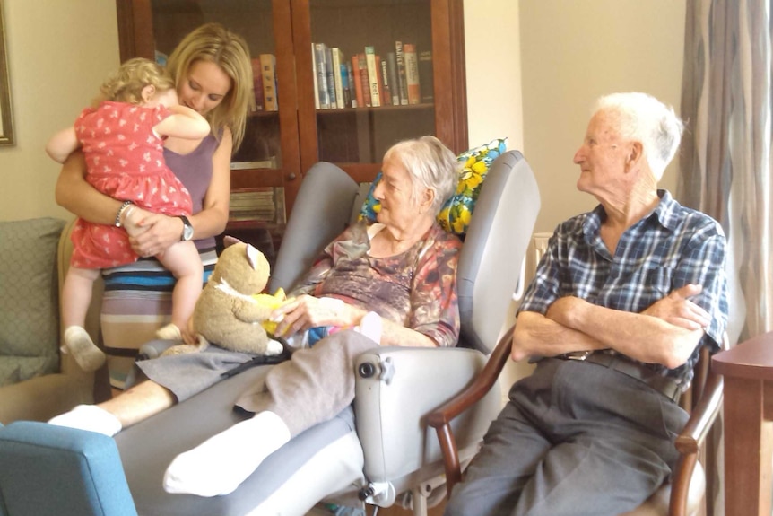 A woman sits in a chair between a man and another woman.