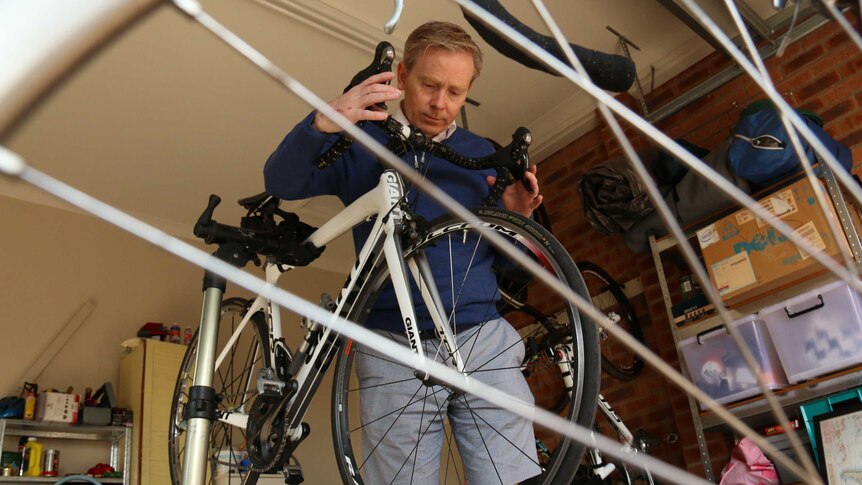 Damien O'Donovan is seen through the spokes of a bike, examining another bike.