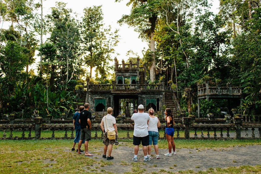 A group of people gather around a castle in a rainforest