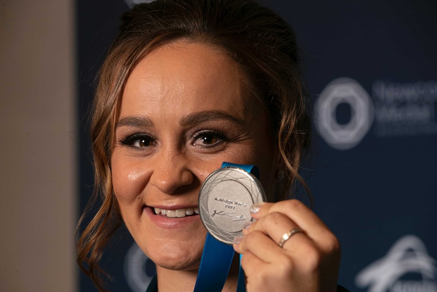 A close up of Ash Barty smiling and holding up the Newcombe Medal.