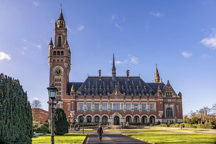 Huge, ornate orange stone building with large turret, a row of lower arched windows and higher rectangle ones, from afar.