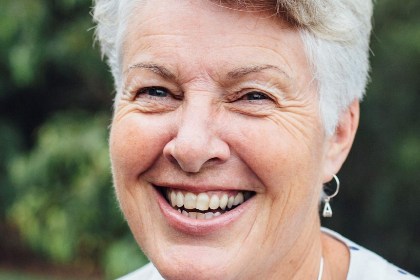 Edwina Aubin with grey hair and a green leafy background.