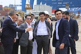 Men in suits stand at a port.