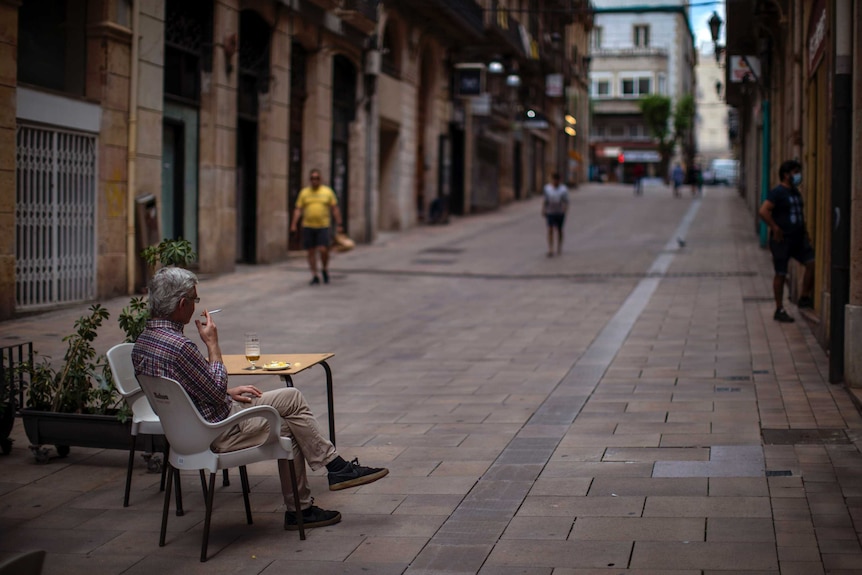 A man sits at a small table on a paved path.