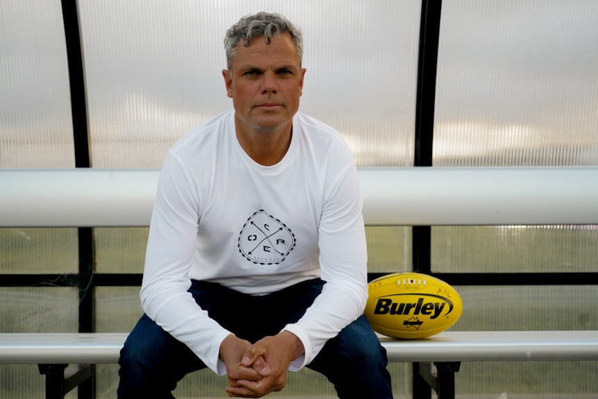 A man sits on a bench next to a football.