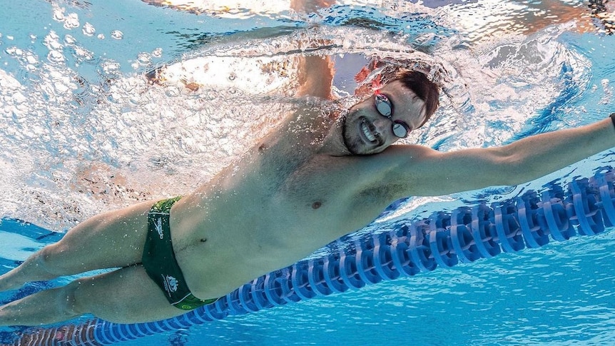 A para-athlete smiles as he swims in a pool.