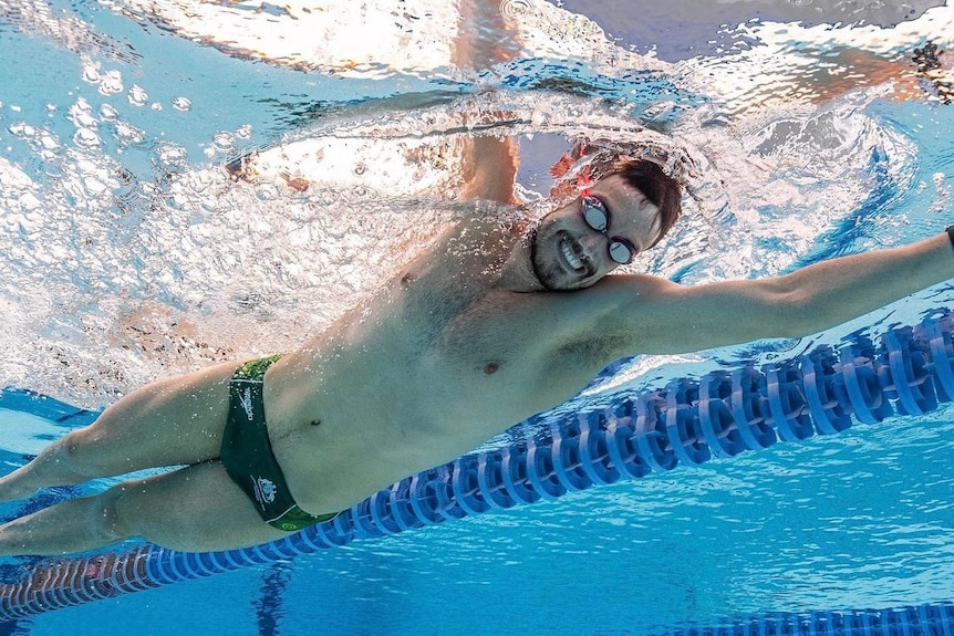 man smiling at camera as he swims in pool