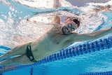 A para-athlete smiles as he swims in a pool.