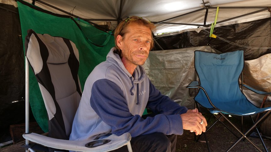 A man sitting under a tarp annex in a camping chair
