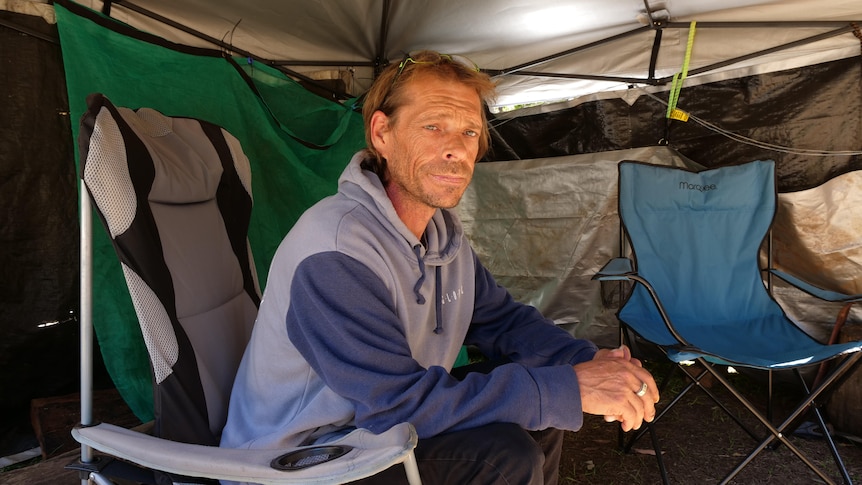 A man sitting under a tarp annex in a camping chair