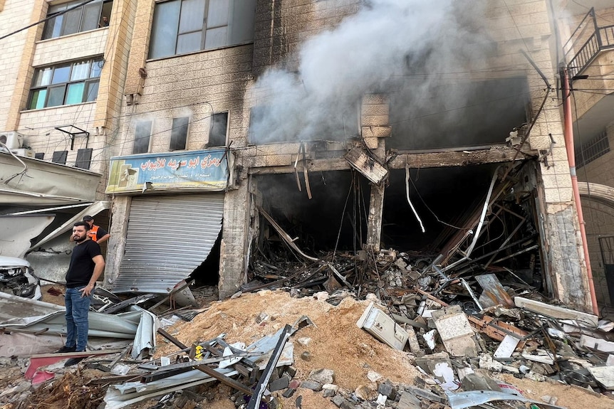 A Palestinian stands next to a destroyed building.