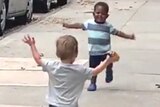 Two toddlers, one white and one black, run towards each other in New York.