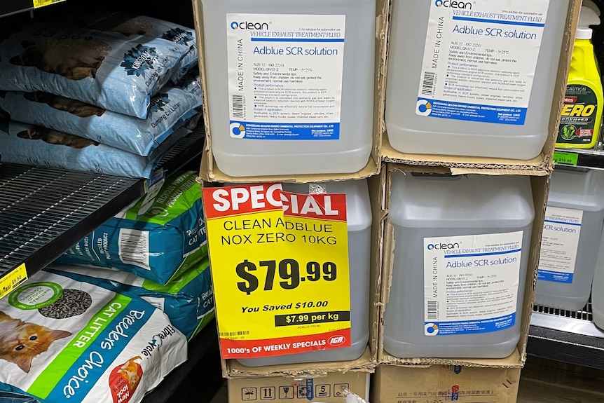 Large drums containing clear fluid stacked on top of each other in front of shelves with a sign advertising its price of $79.99.