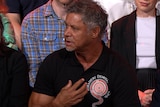 A man in a black shirt gestures with his hand.