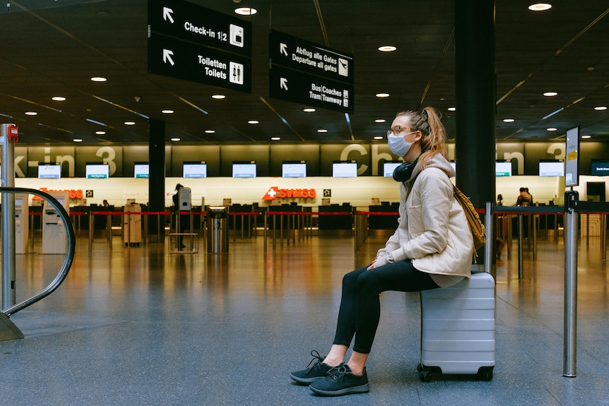 A woman sits on her suitcase in an airport.
