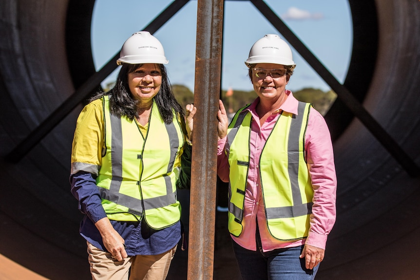 Two women wearing high-vis and hard hats on a construction site.   